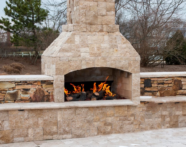 A gas fireplace made from paving stone burning outside on a patio