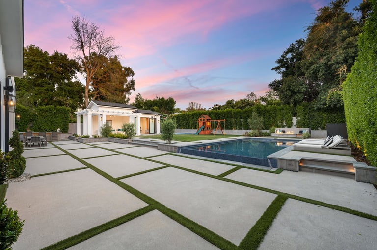 A backyard with concrete pavers, a pool, and grass landscape