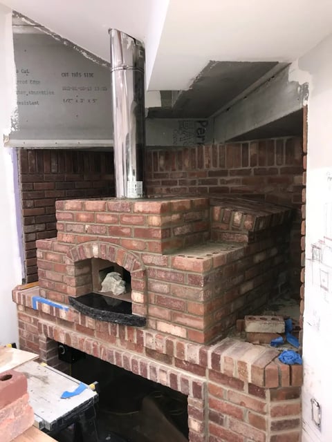 Under-construction brick fireplace with metal ductwork and white panels in an unfinished interior space