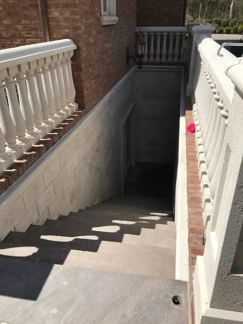 Outdoor stairwell with white railings descending into a narrow brick passage between residential buildings