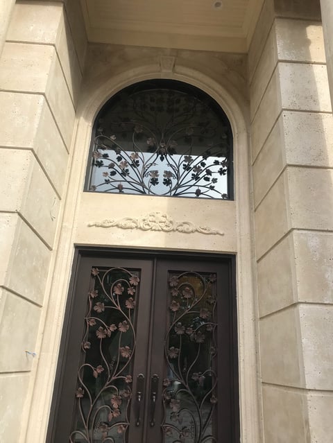 Ornate arched doorway with decorative black metal doors and transom window in cream stone facade