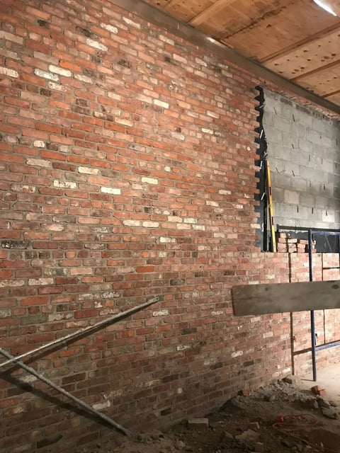 Unfinished basement or construction area with exposed red brick wall and metal shelving unit