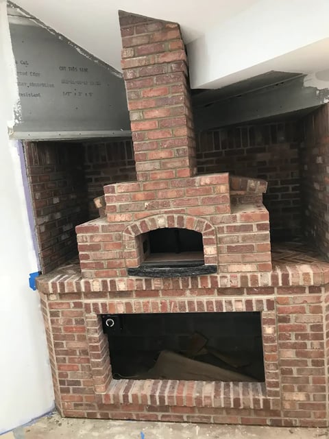 Exposed brick pizza oven and fireplace under construction with metal framework visible above