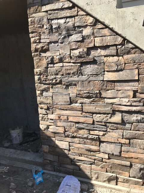 Stack of tan and brown stacked stone blocks on exterior wall with sunlight casting shadows