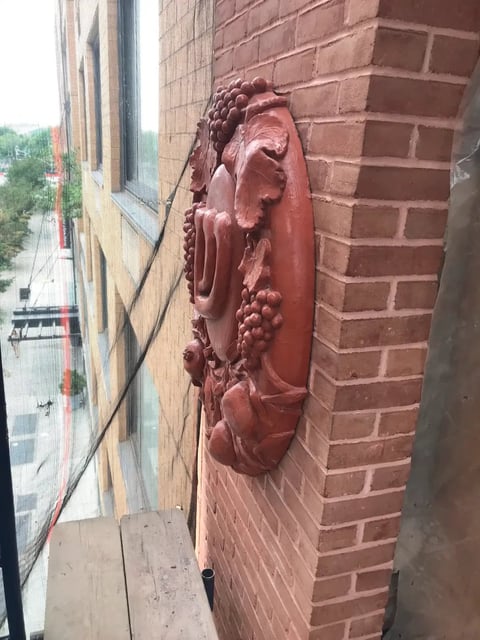 Terracotta architectural ornament of a womans face with grapes mounted on a red brick building exterior