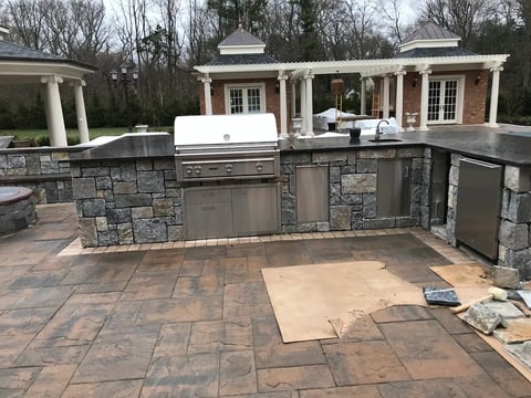 Luxury outdoor kitchen with stone counters, built-in grill, and covered dining pavilion on brick patio