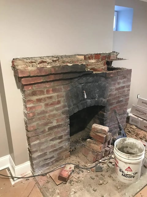 Deteriorated brick fireplace under renovation with exposed interior, construction debris, and tools on the floor