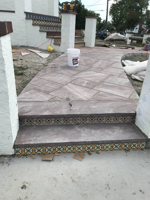 Construction site with decorative tile steps leading to a paved courtyard area with white pillars and surrounding structures