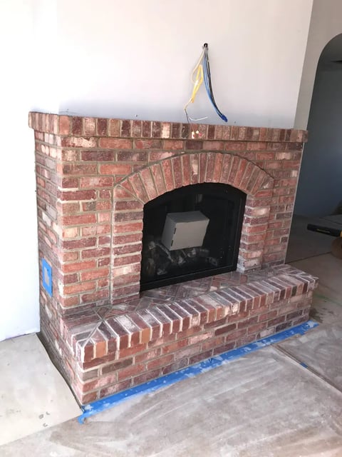New brick fireplace under construction with dark firebox opening and blue painters tape on base