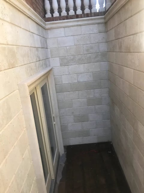 Empty basement stairwell with light-colored concrete block walls, dark floor, and wooden railings visible at the top