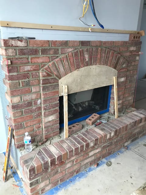Brick fireplace under renovation with arched opening and wooden frame construction in progress
