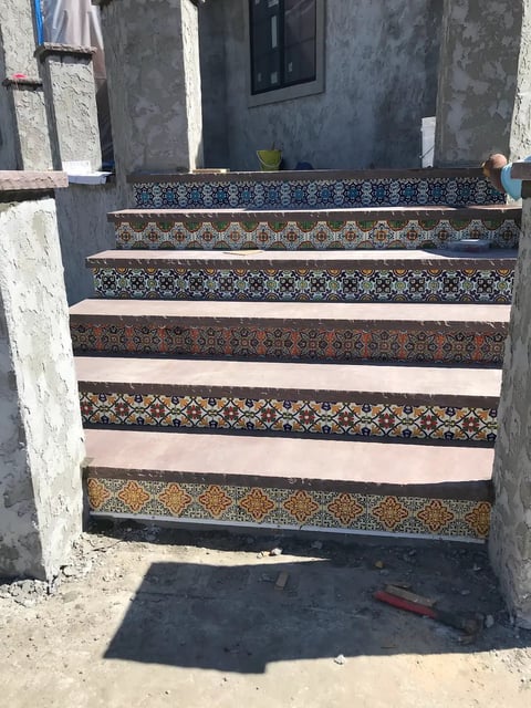 Outdoor staircase with alternating decorative patterned tiles and plain steps leading to a dark doorway on a concrete building