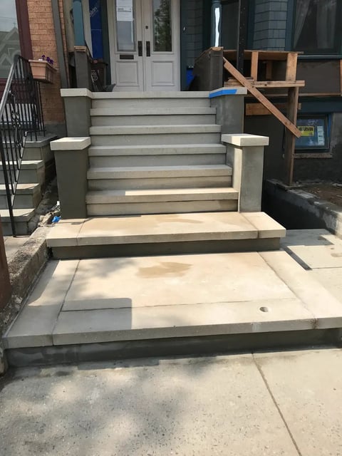Front entrance with concrete steps and metal railings leading to a white double-door building entrance