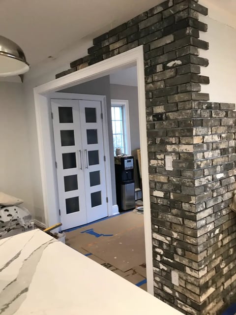 Home interior with white double doors featuring glass panes, dark brick fireplace, and white countertop in foreground