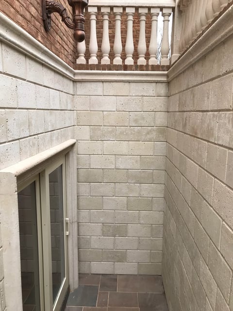 Narrow interior courtyard with beige brick walls, tiled floor, open doorway on left, and decorative wooden railings visible at top
