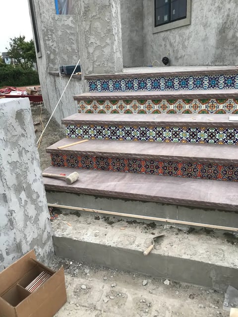 Outdoor staircase with decorative patterned tile trim in blue, white, and earth tones on concrete steps of a weathered building