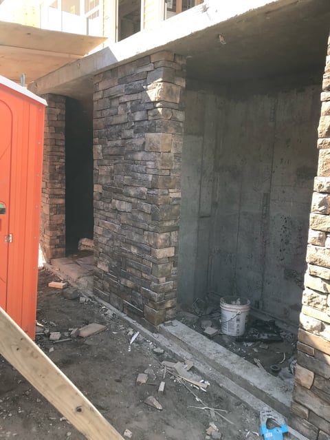 A brick entryway with a red door, concrete floor covered in construction debris, and weathered stone walls, appearing to be under renovation