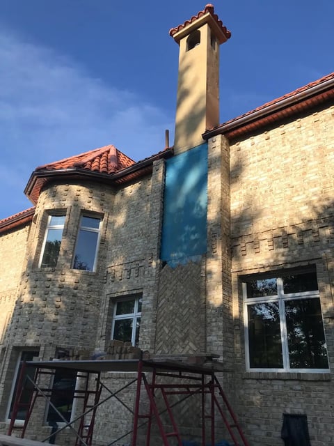 Brick house with tall cream chimney, red tile roof, and large windows under blue sky
