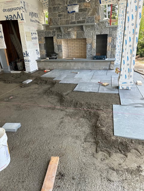 Construction site with concrete fireplace framework, partially laid stone floor tiles, and protective plastic sheeting on exterior walls