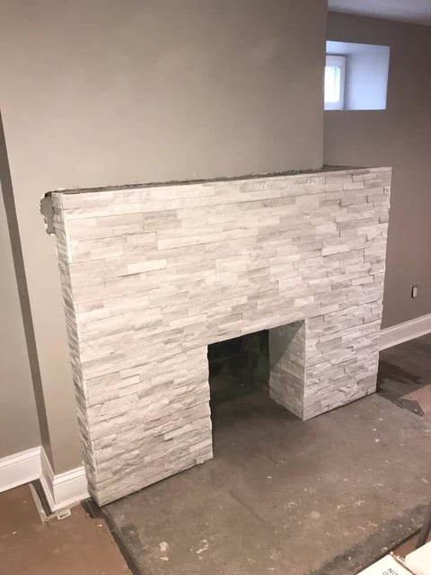 Modern fireplace surround with white stacked stone veneer and dark firebox opening in unfinished basement room