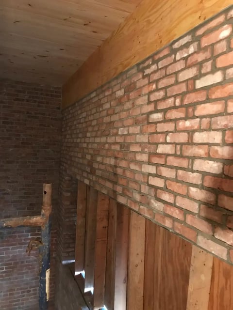 Interior construction space with exposed red brick walls, wooden beam ceiling, and wooden door frames under renovation