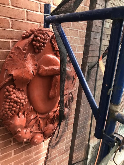 Terracotta fruit relief sculpture mounted on brick wall next to blue metal railing