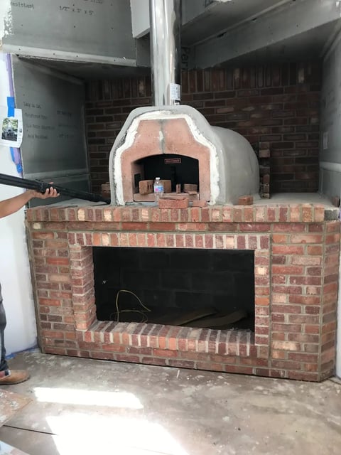 Custom-built brick pizza oven with white dome top in indoor kitchen space, with wood-fired cooking chamber
